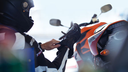 Sediaci jazdec, ktor&yacute; si uťahuje prav&uacute; rukavicu. Napravo od jazdca sa nach&aacute;dza motocykel &ndash; pohľad zozadu.